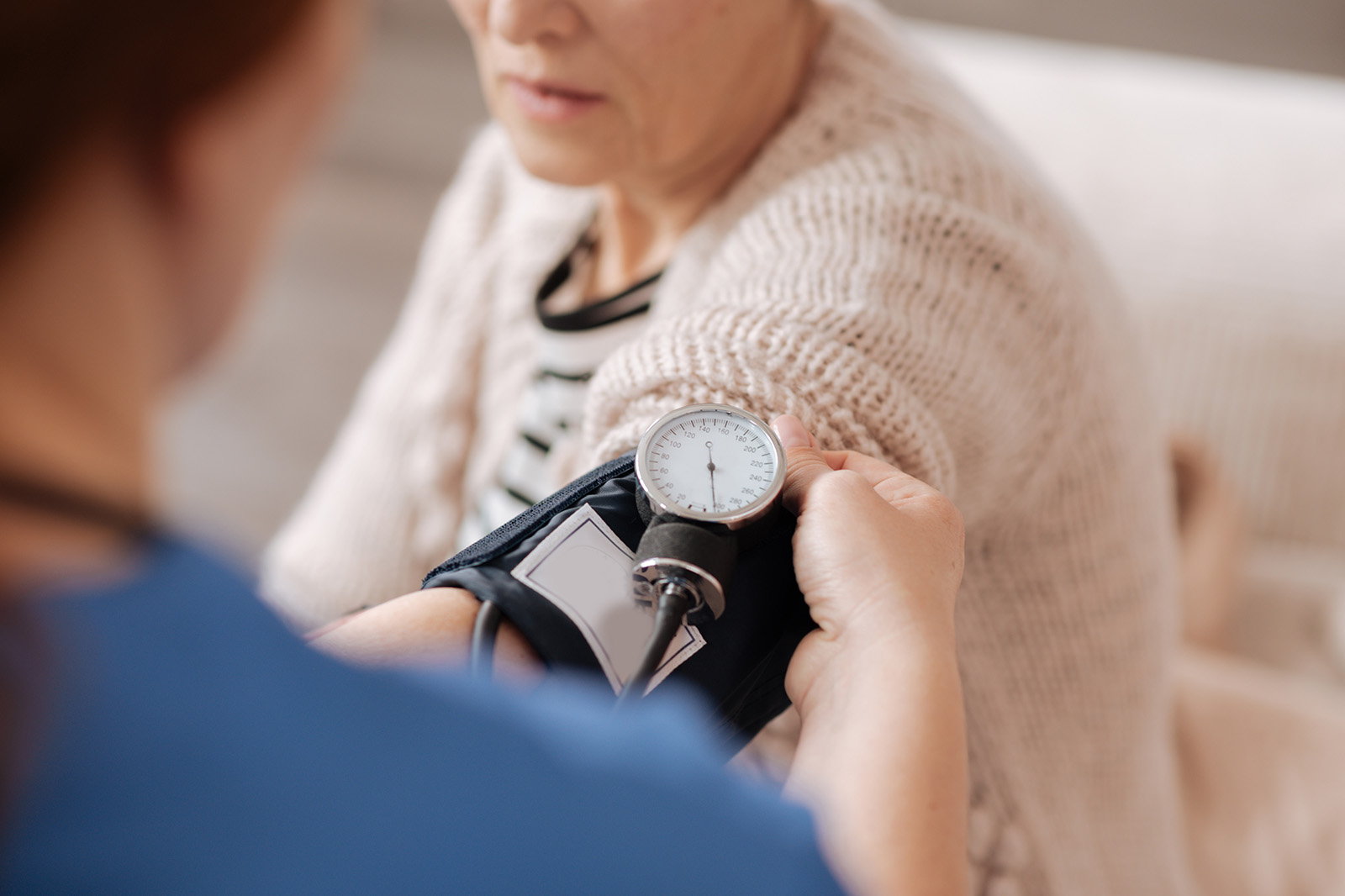 Man sieht im Anschnitt eine ältere Frau, bei der Blutdruck gemessen wird.